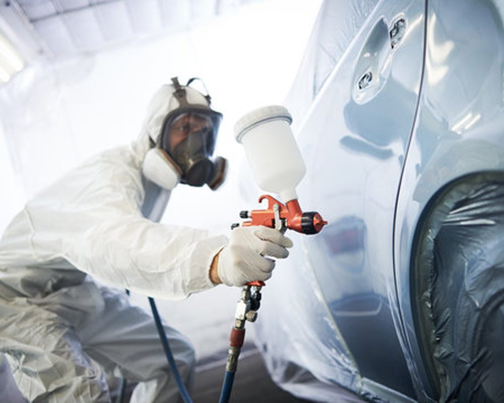 Technician respraying a car panel in a paint booth